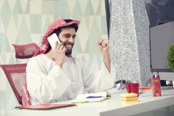 Fiatal Arab üzleti ember beszél a mobiltelefon és a működő pénzügyi költség laptop számítógép. — Stock Fotó
