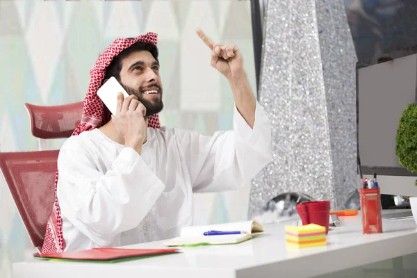 Junger arabischer Geschäftsmann spricht am Handy über Kosten mit Laptop-Computer. — Stockfoto