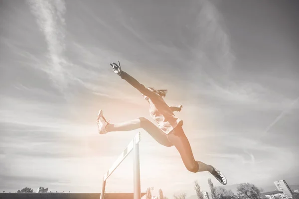 Female athlete jumping above the hurdle during the race — Stock Photo, Image