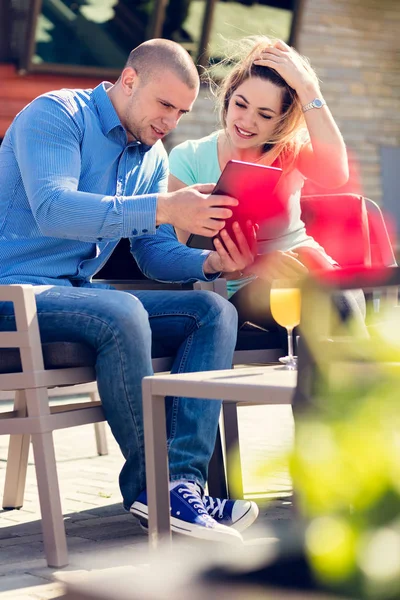 Молодая пара, женщина и мужчина, в уличном кафе пьют кофе и сок во время просмотра фотографий праздников — стоковое фото