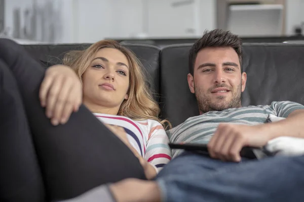 Счастливая молодая пара расслабляется и смотрит телевизор дома . — стоковое фото