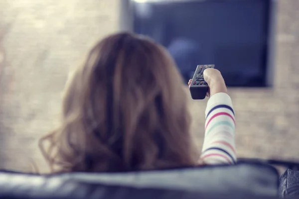 Mulher bonita deitada em um sofá com controle remoto e assistindo televisão — Fotografia de Stock