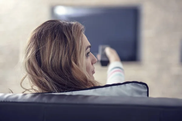 Piękna kobieta leżąca na kanapie z pilotem i oglądająca telewizję — Zdjęcie stockowe