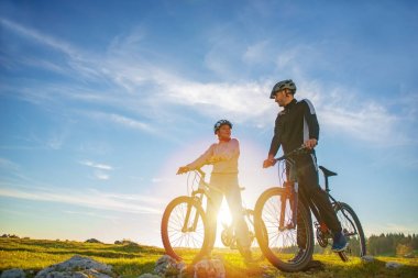 Bisikletçi çift akşam gökyüzü altında tepede duran ve parlak güneş batımında zevk dağ bisikleti ile.