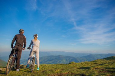Bisikletçi çift akşam gökyüzü altında tepede duran ve parlak güneş batımında zevk dağ bisikleti ile.