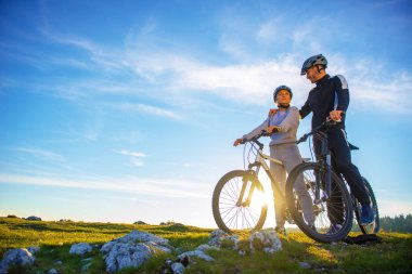 Bisikletçi çift akşam gökyüzü altında tepede duran ve parlak güneş batımında zevk dağ bisikleti ile.