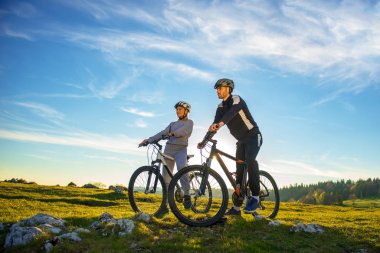 Bisikletçi çift akşam gökyüzü altında tepede duran ve parlak güneş batımında zevk dağ bisikleti ile.