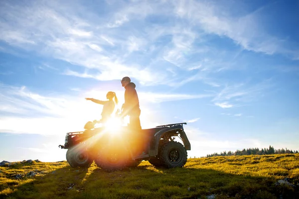 Beautiful couple is watching the sunset from the mountain sitting on atv quadbike — Stock Photo, Image