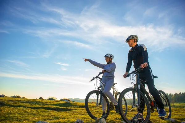 Pareja ciclista con bicicleta de montaña apuntando a la distancia en el campo —  Fotos de Stock