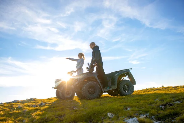 美しいカップルは atv quadbike の上に座って山から夕日を見ています。 — ストック写真