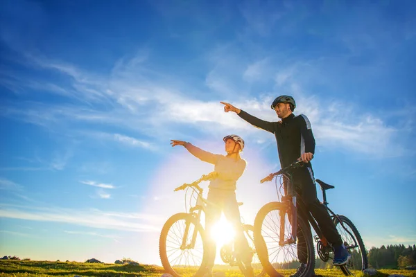 Pareja ciclista con bicicleta de montaña apuntando a la distancia en el campo —  Fotos de Stock