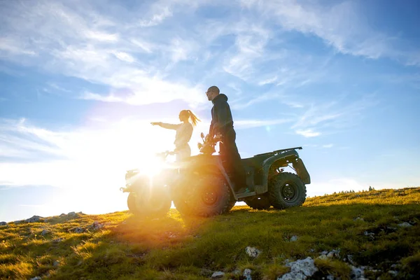 美しいカップルは atv quadbike の上に座って山から夕日を見ています。 — ストック写真