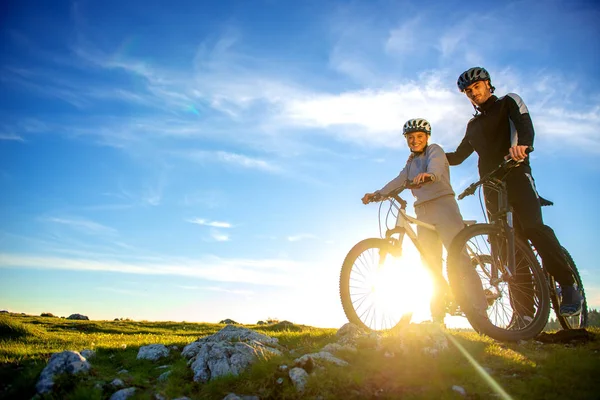 Pareja ciclista con bicicletas de montaña de pie en la colina bajo el cielo de la noche y disfrutando del sol brillante al atardecer . —  Fotos de Stock