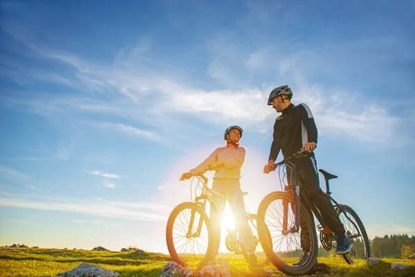 Pareja ciclista con bicicletas de montaña de pie en la colina bajo el cielo de la noche y disfrutando del sol brillante al atardecer . —  Fotos de Stock