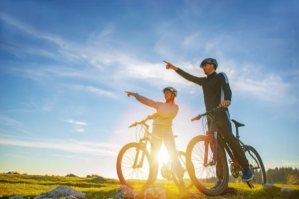Ποδηλάτης ζευγάρι με ποδήλατο βουνού, επισημαίνοντας σε απόσταση στο ύπαιθρο — Φωτογραφία Αρχείου