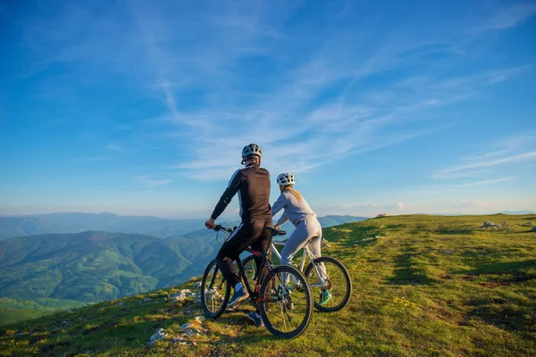 Pareja ciclista con bicicletas de montaña de pie en la colina bajo el cielo de la noche y disfrutando del sol brillante al atardecer . —  Fotos de Stock