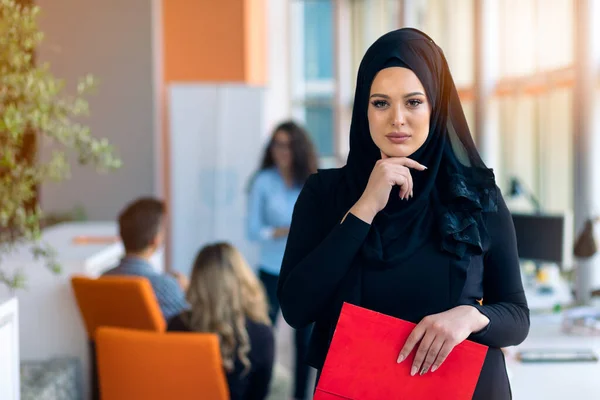 Cheerful woman in the office, holding folder with documents and giving a bright smile. Muslim women employment. — Stock Photo, Image