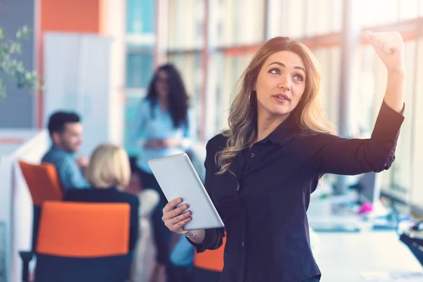 Retrato de mujer de negocios feliz sosteniendo tableta digital en la oficina de pie delante de colegas discutiendo en segundo plano —  Fotos de Stock