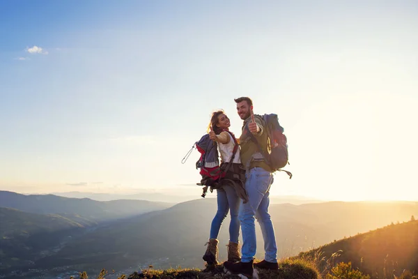 Feliz pareja hombre y mujer turista en la cima de la montaña al atardecer al aire libre durante una caminata en verano —  Fotos de Stock