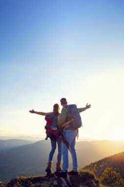 Sırt çantalı yürüyüşçüler bir dağın tepesinde dinleniyorlar ve vadinin manzarasının tadını çıkarıyorlar.