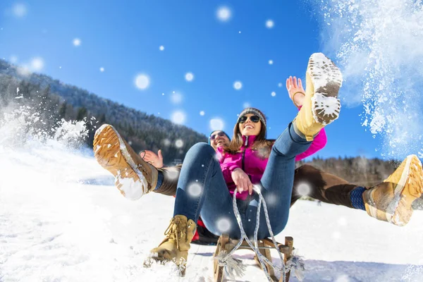 Молодая счастливая пара катается на санках зимой в горнолыжном центре — стоковое фото