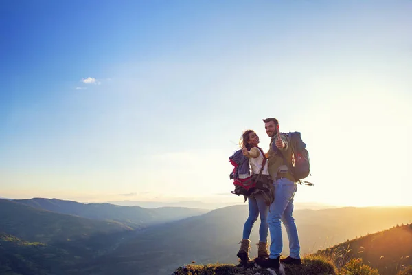 Lyckligt par man och kvinna turist på toppen av berget vid solnedgången utomhus under en vandring på sommaren — Stockfoto