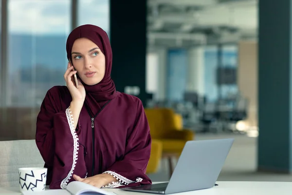 Boldog muszlim üzletasszony hidzsábban az irodában. Mosolygó arab nő dolgozik laptop és beszél okostelefon — Stock Fotó