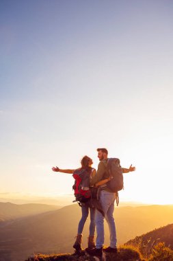 Sırt çantalı yürüyüşçüler bir dağın tepesinde dinleniyorlar ve vadinin manzarasının tadını çıkarıyorlar.