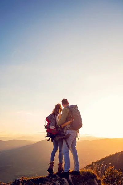 Туристи з рюкзаками відпочивають на вершині гори і насолоджуються видом на долину — стокове фото
