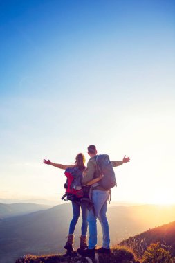 Sırt çantalı yürüyüşçüler bir dağın tepesinde dinleniyorlar ve vadinin manzarasının tadını çıkarıyorlar.