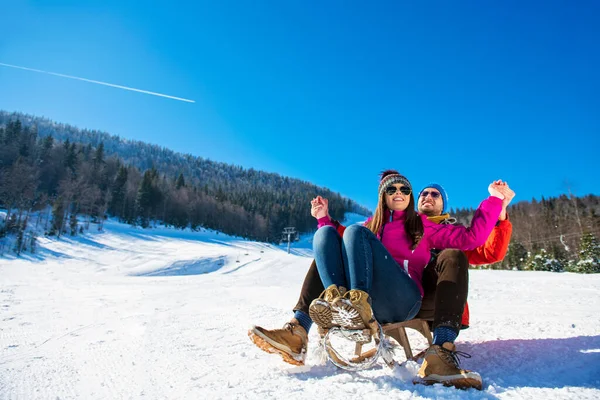 Молодая счастливая пара катается на санках зимой в горнолыжном центре — стоковое фото