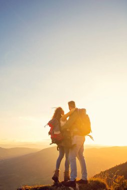 Sırt çantalı yürüyüşçüler bir dağın tepesinde dinleniyorlar ve vadinin manzarasının tadını çıkarıyorlar.