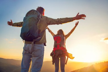 Kollarını kaldırıp el ele tutuşan ve gün batımını izleyen çift.