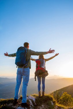 Kollarını kaldırıp el ele tutuşan ve gün batımını izleyen çift.