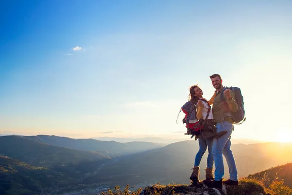 Feliz casal homem e mulher turista no topo da montanha ao pôr do sol ao ar livre durante uma caminhada no verão — Fotografia de Stock