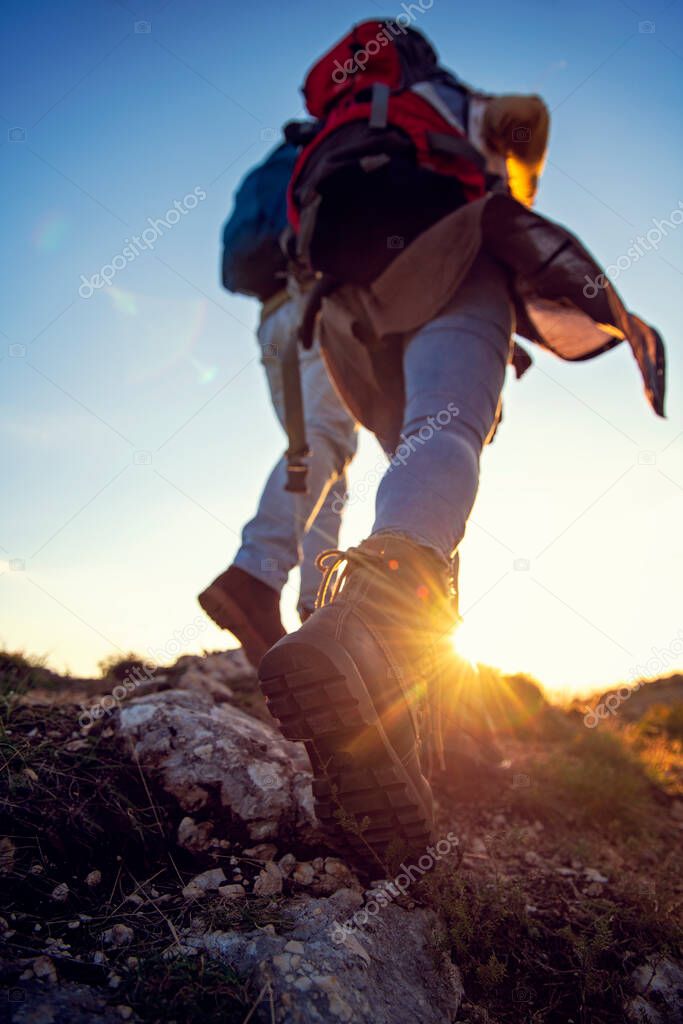 Tourist couple wearing hiking boots walk up a grassy hill in Alps.