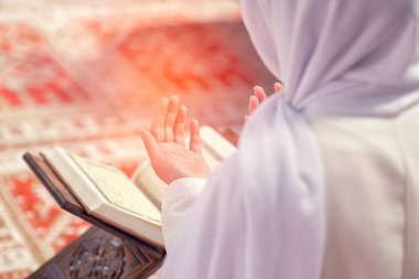 Camide Kur 'an okuyan genç Müslüman kadın ve pencereden düşen güneş ışığı.