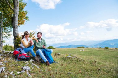 Genç çift dağlarda seyahat ederken kayanın üzerinde dinlenirken su içiyor.