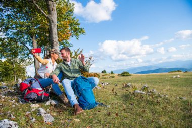 Neşeli genç çift dağlarda seyahat ederken dışarıda selfie çekiyorlar.