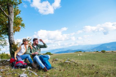 Genç çift dağlarda seyahat ederken kayanın üzerinde dinlenirken su içiyor.