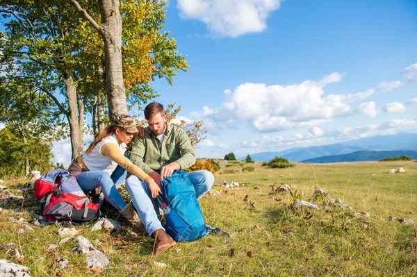 Genç çift dağlarda seyahat ederken kayanın üzerinde dinlenirken su içiyor.