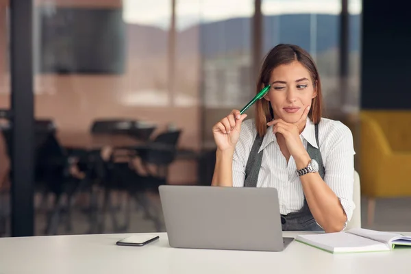 Giovane donna annoiata vestita con camicia seduta sul posto di lavoro — Foto Stock