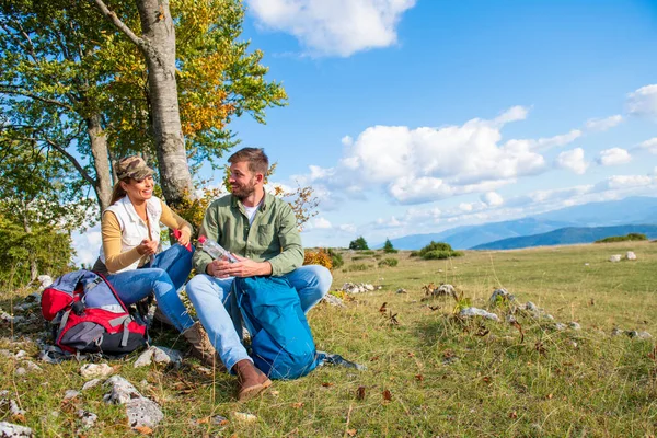 Genç çift dağlarda seyahat ederken kayanın üzerinde dinlenirken su içiyor.