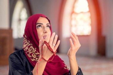 Camide Kur 'an okuyan genç Müslüman kadın ve pencereden düşen güneş ışığı.