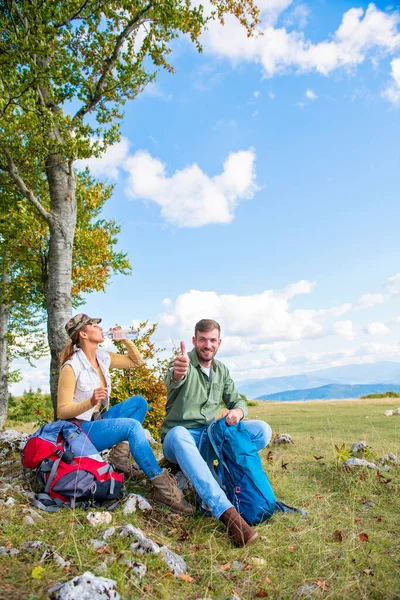 Mladý pár pitná voda při odpočinku na skále během cesty v horách — Stock fotografie