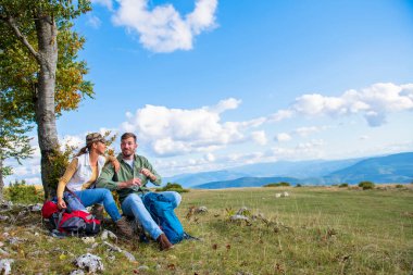 Genç çift dağlarda seyahat ederken kayanın üzerinde dinlenirken su içiyor.