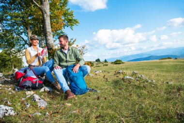 Genç çift dağlarda seyahat ederken kayanın üzerinde dinlenirken su içiyor.