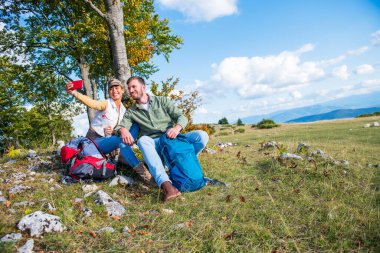 Neşeli genç çift dağlarda seyahat ederken dışarıda selfie çekiyorlar.