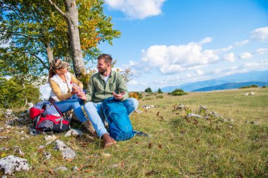Genç çift dağlarda seyahat ederken kayanın üzerinde dinlenirken su içiyor.