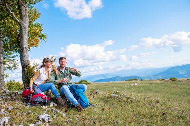 Genç çift dağlarda seyahat ederken kayanın üzerinde dinlenirken su içiyor.